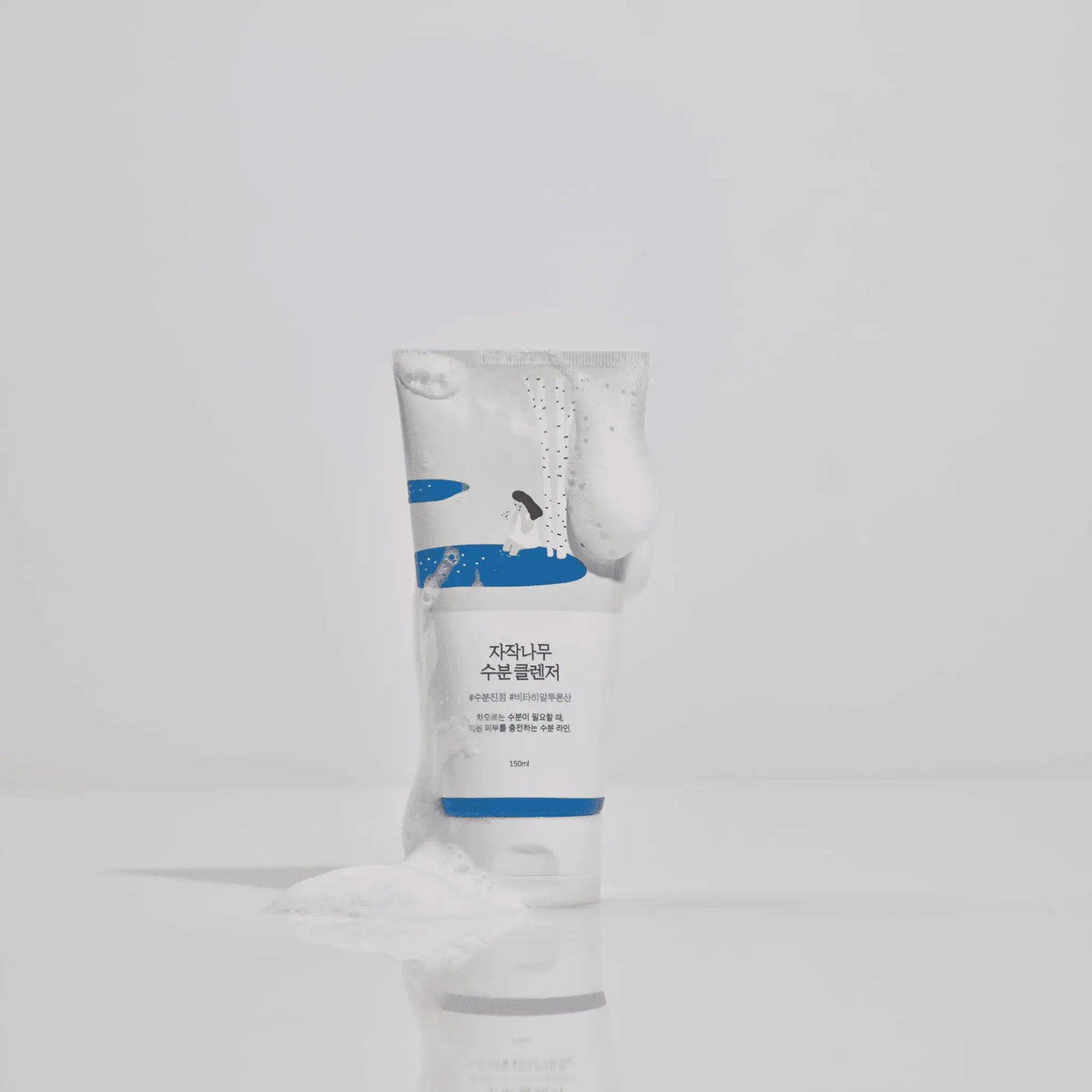 ROUND LAB Birch Juice Moisturizing Cleanser 150 ml tube covered with foam on a reflective surface — manufacturer photograph